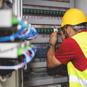 Electrician engineer work tester measuring voltage and current of power electric line in electical cabinet control.