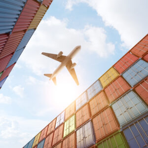 Cargo plane flying above stack of containers at container port