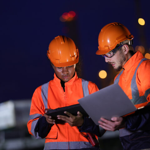 Male and female engineers in orange safety uniforms work together at night ship at the refinery plant