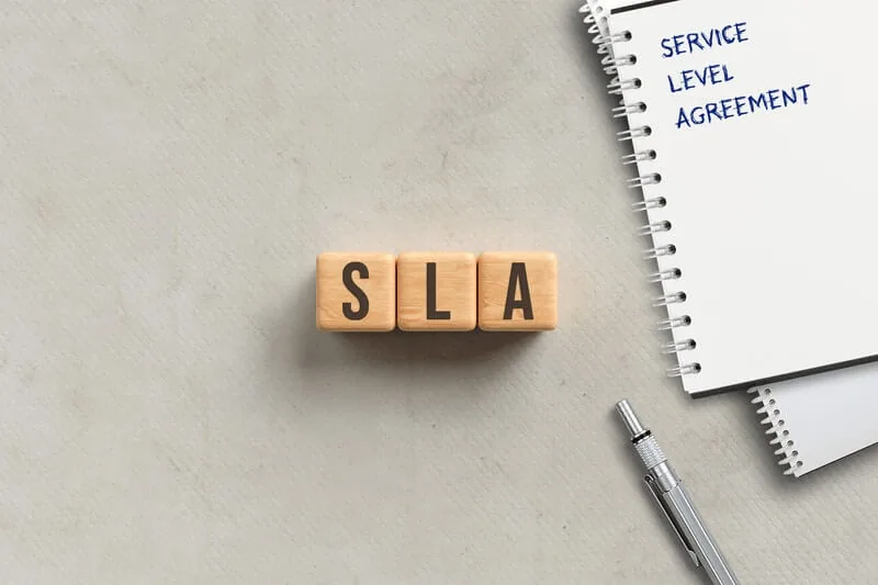 Wooden blocks spelling SLA beside a notepad headed Service Level Agreement