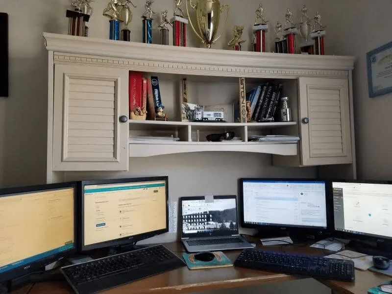 Home office desk with multiple monitors, a laptop and a shelf of trophies