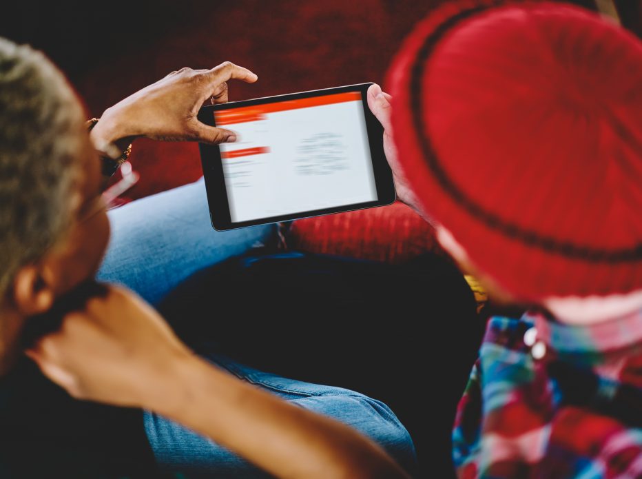 Cropped back view of couple in love holding touch pad device and choosing movie on internet websites using wireless 4G connection.Young marriage updating software to install app on digital tablet