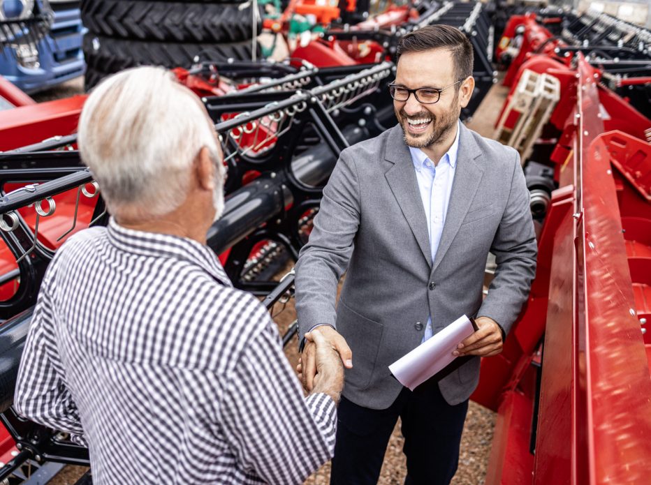 Farmer and tractor salesman shaking hands and discussing about financial plans.