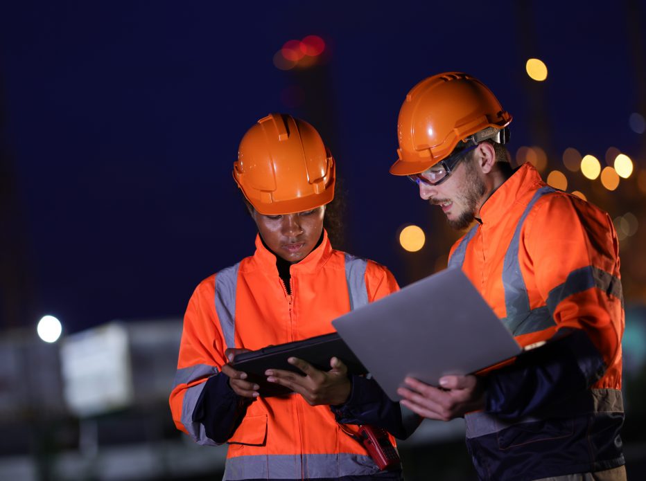 Male and female engineers in orange safety uniforms work together at night ship at the refinery plant