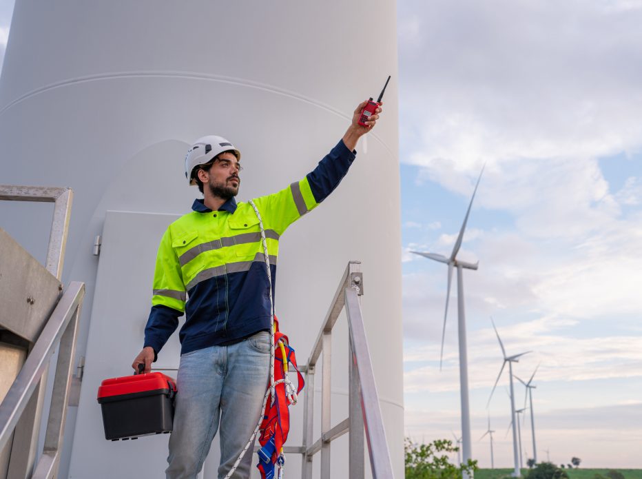 Engineer wearing uniform inspection and survey work in wind turbine farms rotation to generate electricity energy. Maintenance engineer working in wind turbine farm at sunset.