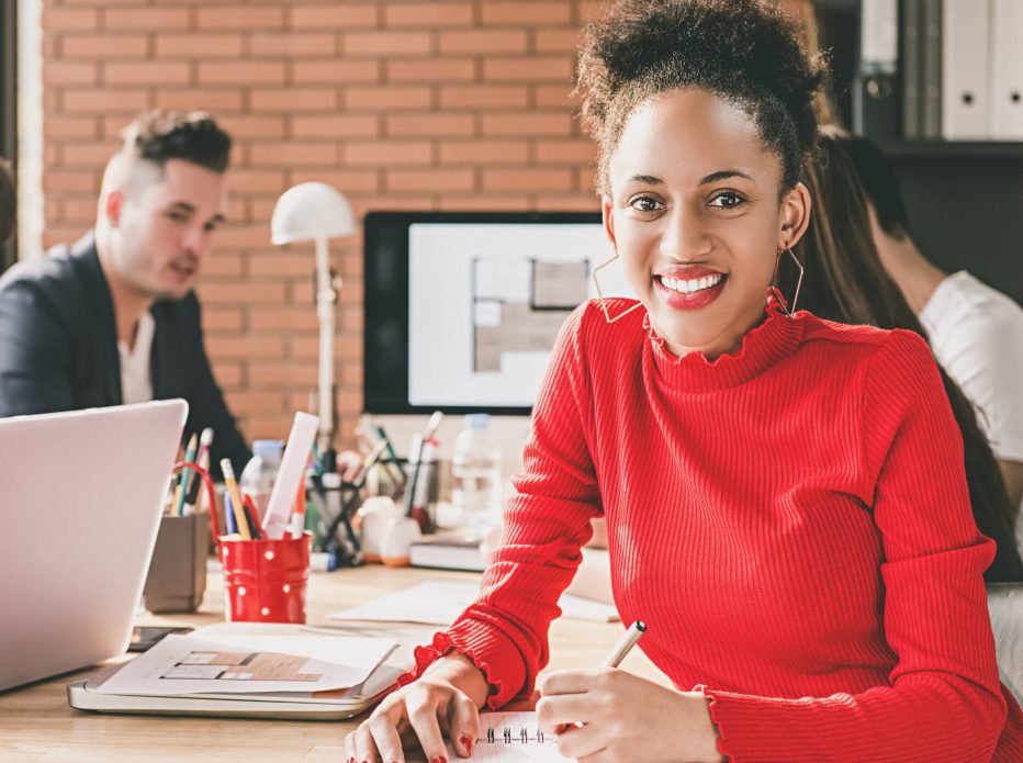 Young casual beautiful black businesswoman writing in her notebook at an office meeting with her interior designer team